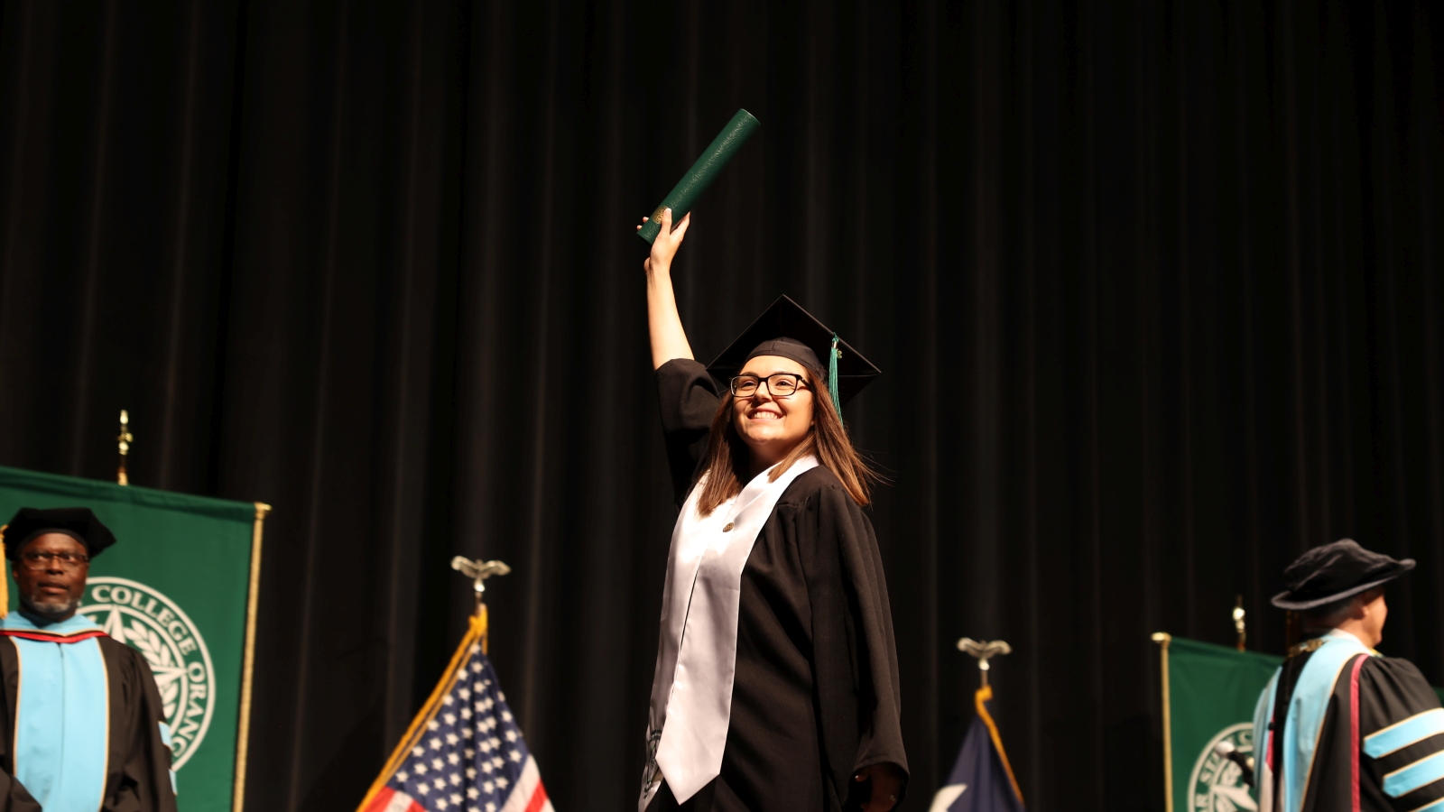 Student holding up diploma walking across Commencement stage